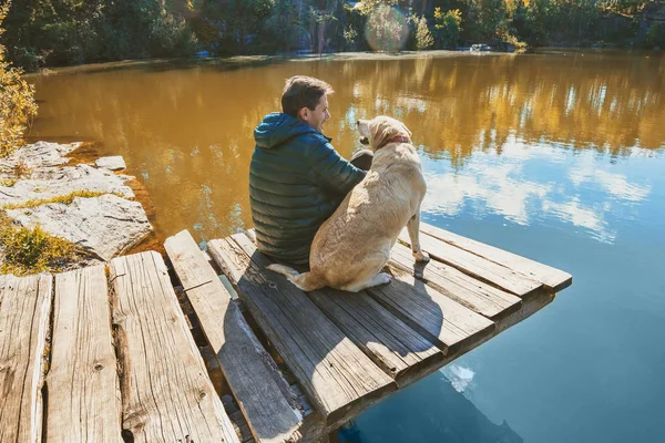 Человек Собакой Лабрадором Сидит Деревянной Палубе Красивом Скалистом Берегу Озера — стоковое фото