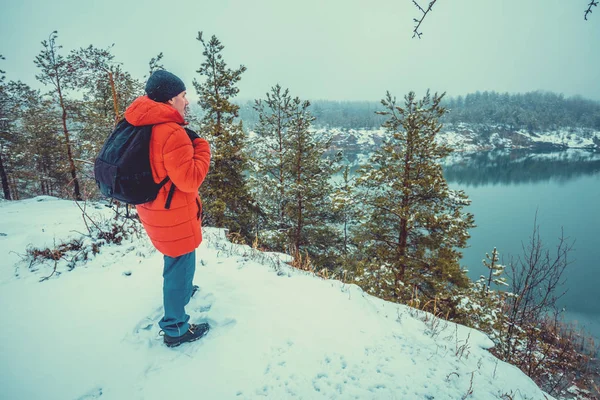 Stock image A man standing on the covered with snow rocky lakeshore in winter and looking at the beautiful lake