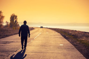 Bir adam bir altın gün batımında deniz boyunca bir beton yol boyunca yürür ve dağ görünüyor