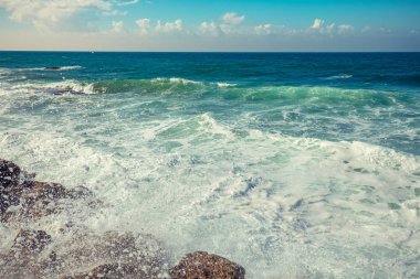 Kayalık sahilde deniz dalga köpüğü. Sahilde okyanus dalgası. Güneşli bir sahil. Rüzgarlı hava