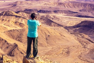 Çölde uçurumun kenarında duran ve fotoğraf çeken bir adam.