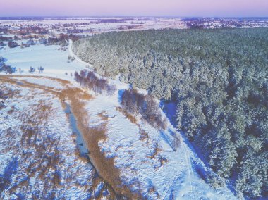 Akşam kış kırsal manzara üst görünümü. Karla kaplı tarlalar, orman ve donmuş dere