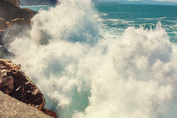 A huge wave is breaking on the rocks. Splash of the wave. Rocky seashore. Beautiful nature, landscape, stormy sea. San Sebastian, Basque Country, Spain, Europe