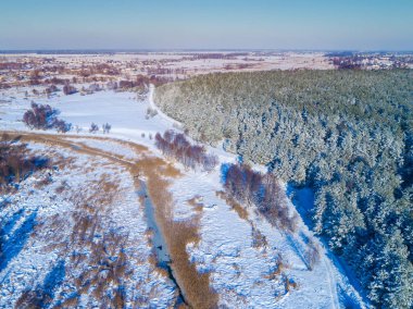 Akşam kış kırsal manzara üst görünümü. Karla kaplı tarlalar, orman ve donmuş dere
