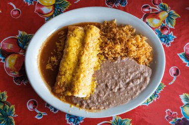 Traditional Mexican style meal with rice, refried beans, burrito, and enchilada. clipart