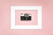 Plocha ležel starý analogový fotoaparát v papírovém rámečku na růžovém pozadí