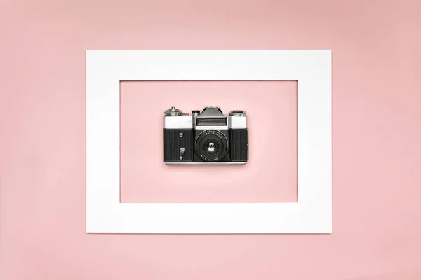 Flat lay old analog camera in the paper frame on pink background