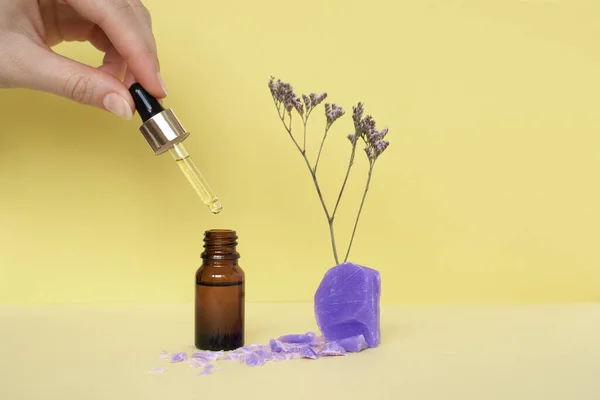 Cosmetic bottle with oil or serum and female hand holding pipette with soup and flower on yellow background — Stock Photo, Image