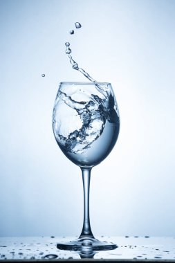 Mavi arka planda su sıçraması. Sulu şarap bardağı..