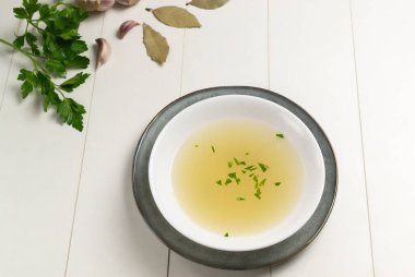 Beyaz bir tabakta taze et suyu. Beyaz arka planda maydanozlu ve sarımsaklı bitkiler. Et, havuç, soğan, sarımsak, maydanoz ve biberden yapılmış sıcak çorba. Seçici odak Kopyalama alanı.