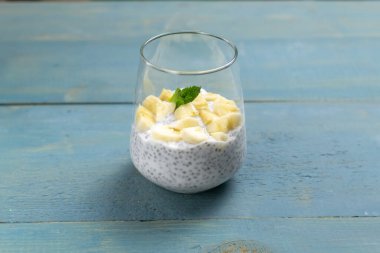 Mavi ahşap arka planda cam bir fincanda naneli Chia pudingi. Uzayı kopyala Sağlıklı bir atıştırmalık yoğurt ve tahıldan oluşur; nane aroma için eklenebilir. Dikey oryantasyon. Seçici odak