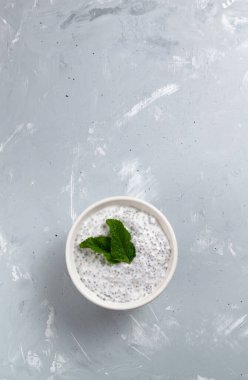Gri arka planda beyaz bir kasede nane yapraklı Chia pudingi. Üst Manzara. Sağlıklı bir kahvaltı yoğurt ve chia fasulyesinden oluşur. Boşluğu kopyala.