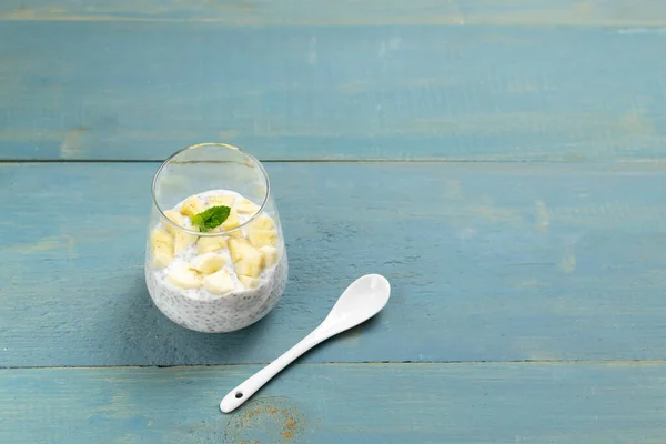 Chia pudding with a sprig of mint in a glass cup with a teaspoon on a blue wooden background. Copy space. A healthy breakfast consists of yogurt and grains, mint can be added for flavor. Horizontal orientation. Selective focus
