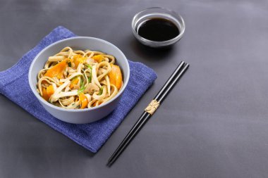 Tavuklu Udon eriştesi, soya sosu ve siyah arka planda mavi bir peçete üzerinde bambu çubukları. Japon mutfağı..