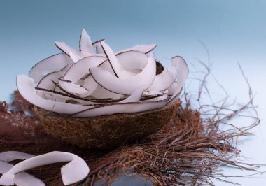 Açık mavi arka planda kurutulmuş palmiye yaprağı üzerinde ev yapımı hindistan cevizi cipsi. Mutfakta hazırlanmış doğal atıştırmalıklar..