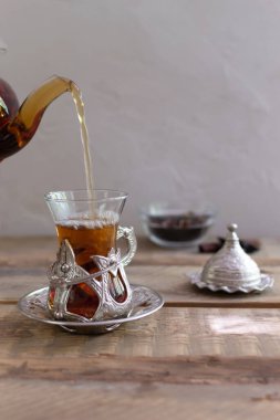 Ahşap bir masada geleneksel cam bir fincanda Türk çayı. Çay dökme işlemi. Uzayı kopyala Dikey yönelim.
