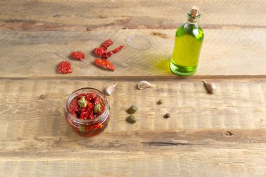 Cam kavanozda güneşte kurutulmuş domatesler, ahşap arka planda baharatlar ve kapariler. Yatay yönelim.
