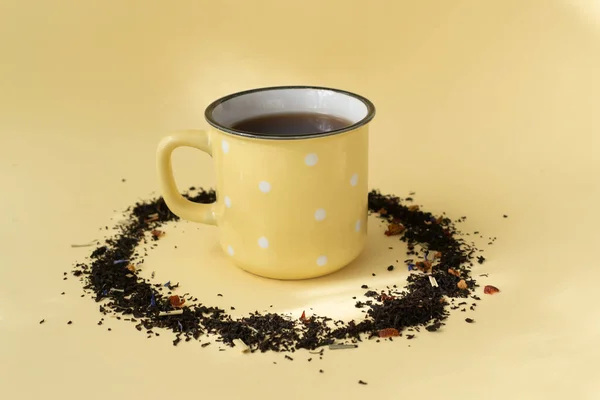 黄色の背景に散在乾燥茶とセラミック黄色のカップに黒茶のカップ スペースのコピー — ストック写真