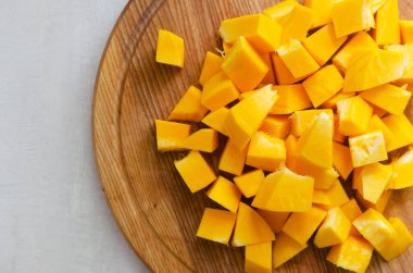 Gri bir masada tahta bir tahtanın üzerinde balkabağı küp şeklinde kesilmiş. Yemek pişirme süreci. Sonbahar yemeği. Seçici odaklanma. Yatay oryantasyon. Üst Manzara. Boşluğu kopyala