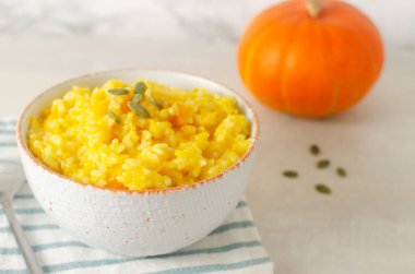 Gri bir masanın üzerinde çizgili bir peçete üzerinde beyaz ve turuncu bir kasede balkabaklı risotto. İtalyan yemeği konsepti. Sonbahar yemeği. Seçici odaklanma. Yatay oryantasyon. Boşluğu kopyala