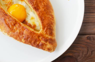 Mutfaktaki ahşap bir masada gri bir tabakta yumurta sarısı olan Adjarian Khachapuri. Geleneksel Gürcü hamur işleri kavramı. Yatay oryantasyon. Üst görünüm