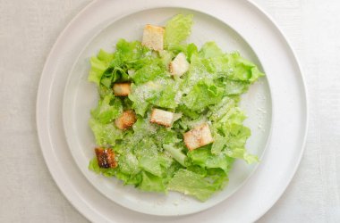 Geleneksel Sezar salatası, kızarmış ekmek ve seramik düz tabakta parmesan peyniri ve gri bir masada malzemeler. Geleneksel Amerikan mutfak konsepti. Dikey oryantasyon. Seçici odaklanma. Üst görünüm.