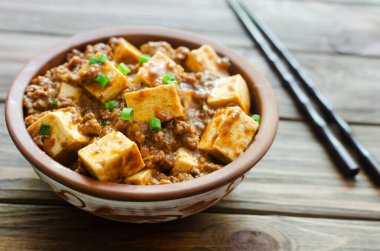Baharatlı soslu Mapo tofu tabağı ve ahşap bir arka planda seramik kasede kıyma. Sichuan bölgesinden bir tabak. Geleneksel Asya yemekleri. Seçici odaklanma. Yatay yönelim.