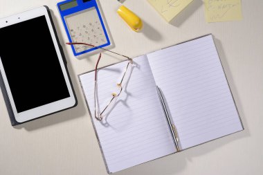 defter gözlük kalem tablet ve bir hesap makinesi masaya vardır