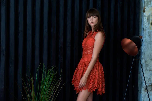 Menina em um vestido vermelho perto da parede preta — Fotografia de Stock