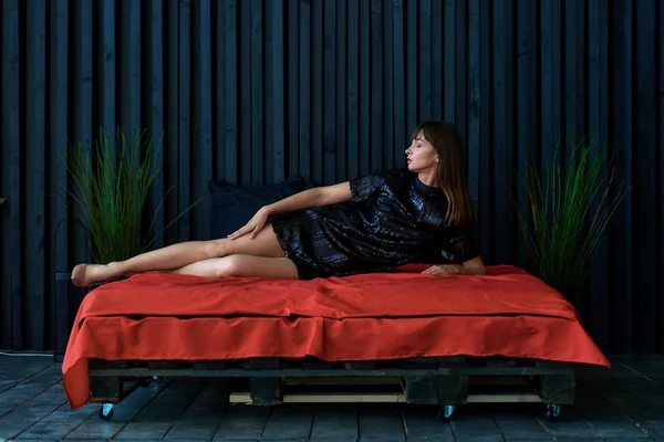 Menina em um vestido preto em uma cama vermelha — Fotografia de Stock