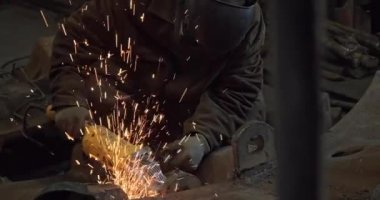 Yakın plan demirci koruyucu maskeli kaynak makinesi metal ve demirle çalışır.