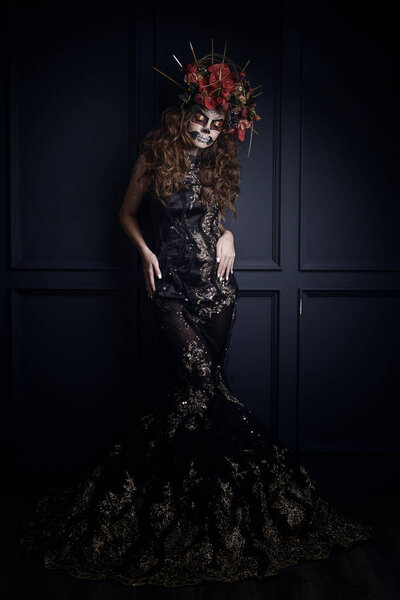 A young beauty woman in the image of an attractive mysterious witch with black hair. Creative makeup for Halloween party. Black poppy and dark backdrop. Celebrating Dia de los Muertos.