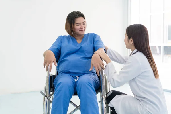 Asian woman Doctor talking to young pregnant woman in wheelchair at hospital. Beautiful asian doctor taking care of patient in wheelchair
