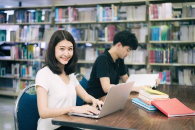 Mutlu çift Asya öğrenciler dizüstü bilgisayar ve kütüphane Üniversitesi'nde konuşan kitap ile. Mutlu arayan kız öğrenci.