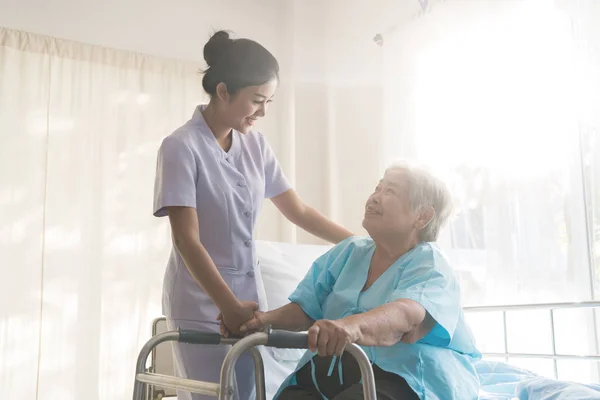 Asian young nurse supporting elderly patient disabled woman in using walker in hospital. Elderly patient care concept