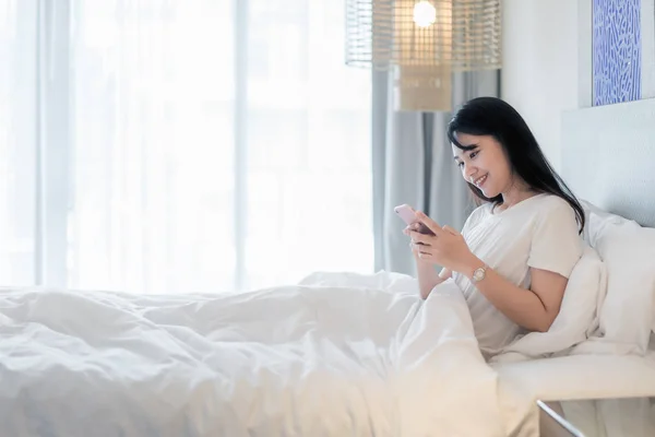 Молодая Улыбающаяся Азиатская Женщина Лежащая Белой Кровати Пользующаяся Телефоном Своей — стоковое фото