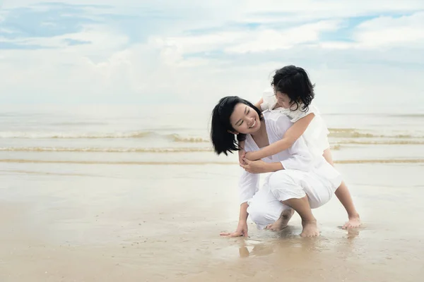 Happy Asian family mother and child daughter hug and play at beach. Happy family summer vacation concept.