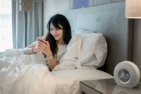 ガジェットでの朝 スマート フォンを使用してベッドに横になっているアジアの美しい若い女性 — ストック写真