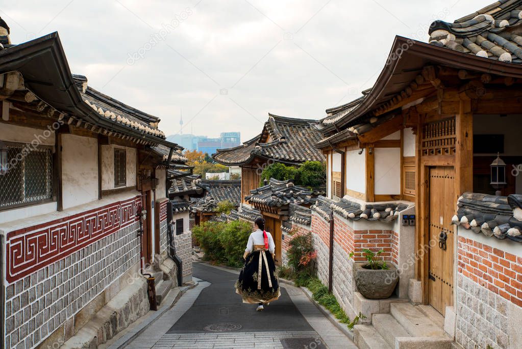 Back of Asian woman wearing hanbok walking through the Seoul traditional style houses of Bukchon Hanok Village in Seoul, South Korea.