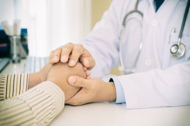 Teşvik için masada oturan hasta el holding samimi adam doktor eller, empati, tezahürat ve destek tıbbi süre sınav. Kötü haber azalmıyor, güven ve etik kavramı