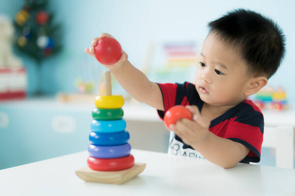 Восприимчивый азиатский мальчик, сидящий на стуле и играющий дома с цветными развивающими игрушками
