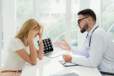 Adam doktor hastaya tanı açıklayan. Arayan kadın hasta yatak haberleri dinlerken endişeli.