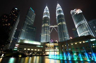 Geceleri gölün kenarındaki renkli çeşme, İkiz Kuleler 'in yanında, arka planda şehir var. Kuala Lumpur, Malezya.