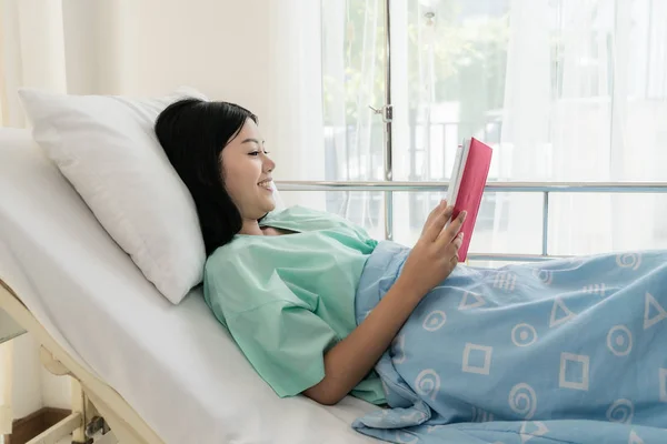 Asiatique jeune femme patient lecture livre tout allongé sur le lit dans — Photo