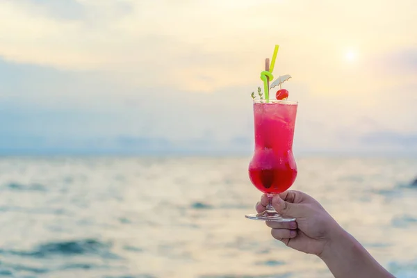 Mão segurando bebida cocktail vermelho no crepúsculo mar & céu fundo — Fotografia de Stock