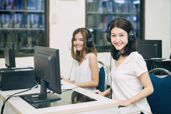 Smiling Asian perempuan mahasiswa berpose dengan komputer sementara studyin — Stok Foto