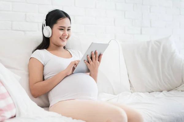 Retrato de mujer embarazada asiática sentada en el sofá en casa y lis — Foto de Stock