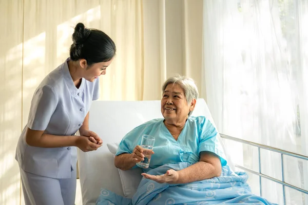 Asiatique infirmière donnant des médicaments et verre d'eau à la femme âgée — Photo