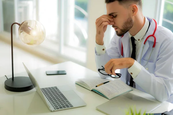 Stressed doctor sitting at his desk in his office while he overw