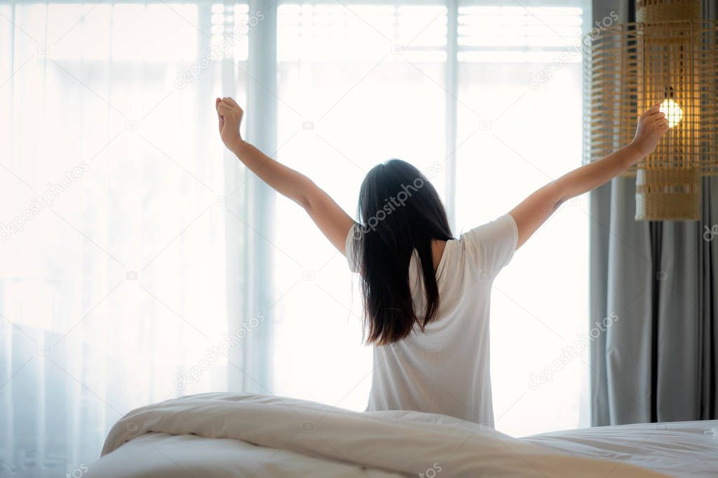 Rear view of Asian Woman stretching hands and body in bed after 